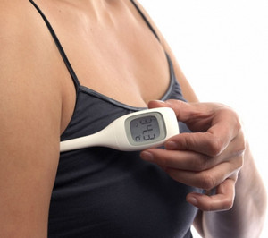 Женщина измеряет температуру тела подмышкой