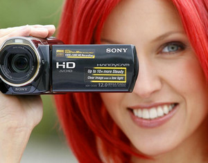 Видеокамера в руках у девушки с красными волосами