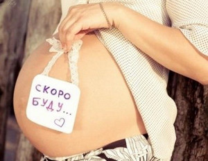 Беременная девушка держит табличку с надписью возле живота
