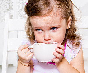 Девочка в розовом платье пьет чай из кружки