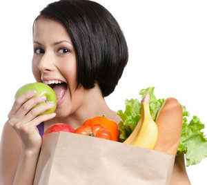 Девушка держит пакет с овощами и ест зеленое яблоко