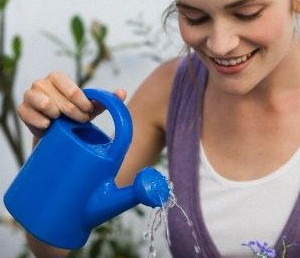 Девушка поливает комнатные растения из синей лейки