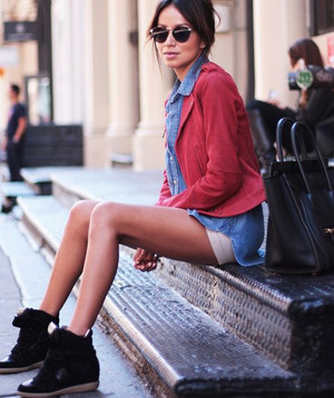 Девушка в красной куртке и черных сникерсах сидит на ступеньках