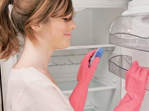 Девушка в розовых резиновых перчатках моет холодильник