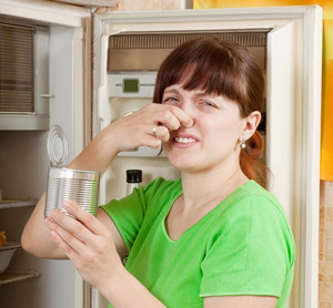 Девушка закрывает нос от запаха из холодильника