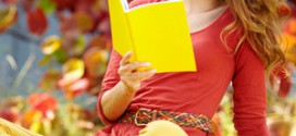 Рыжеволосая девушка в красном платье читает книгу в желтой обложке