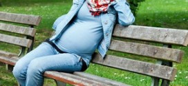 Беременная девушка в синей одежде сидит на лавочке в парке