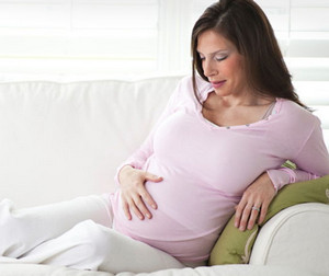 Беременная женщина в розовой кофте сидит на диване