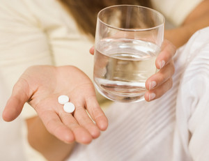 Две таблетки и стакан воды в руках у девушки