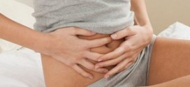 Девушка в серой майке держит руки на животе