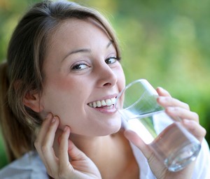 Радостная девушка пьет воду из стакана