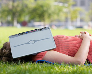 Девушка лежит на траве с ноутбуком на лице