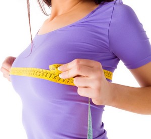Девушка в фиолетовой футболке измеряет грудь сантиметром