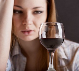 Девушка смотрит на бокал красного вина