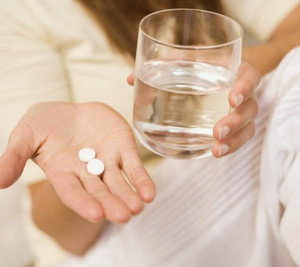 Две таблетки и стакан воды в руках у женщины