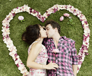 Парень и девушка целуются на траве в сердечке из цветов