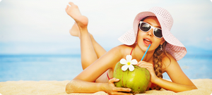 Девушка лежит на пляже и пьет коктейль из фрукта