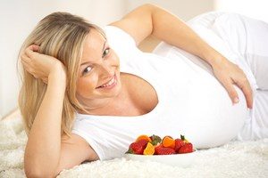 Беременная девушка лежит на кровати, рядом стоят фрукты