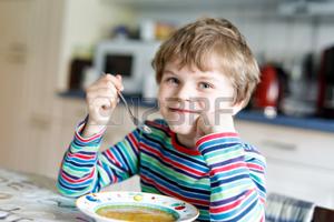 Adorable little school boy eating vegetable soup indoor.