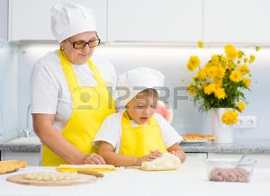 Happy grandmother teaches the child to knead the dough in the kitchen. Фото со стока