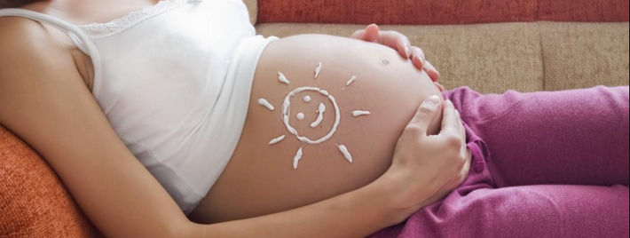 Беременная лежит на диване с солнцем из крема на животе