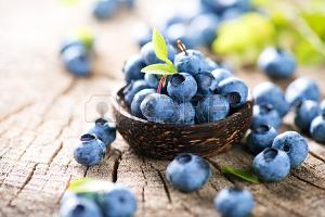 Juicy and fresh blueberries with green leaves in wooden bowl Фото со стока