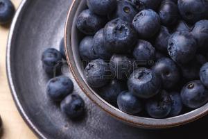 Fresh blueberries in the vintage blue cup on a rustic creamy wooden board