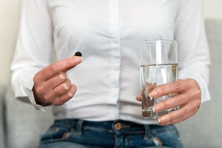 стакан воды и таблетка активированного угля в руках у женщины