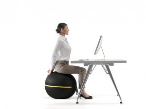 Business woman sitting at desk on Wellness Ball relieving back pain through yoga exercise